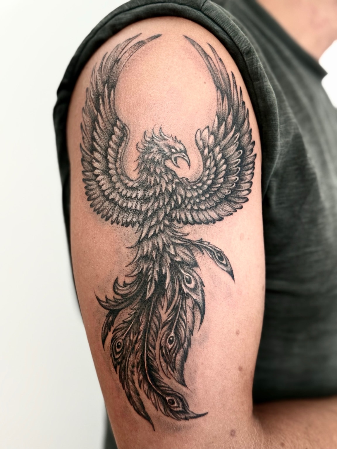 Black and grey phoenix tattoo with open wings on the upper arm