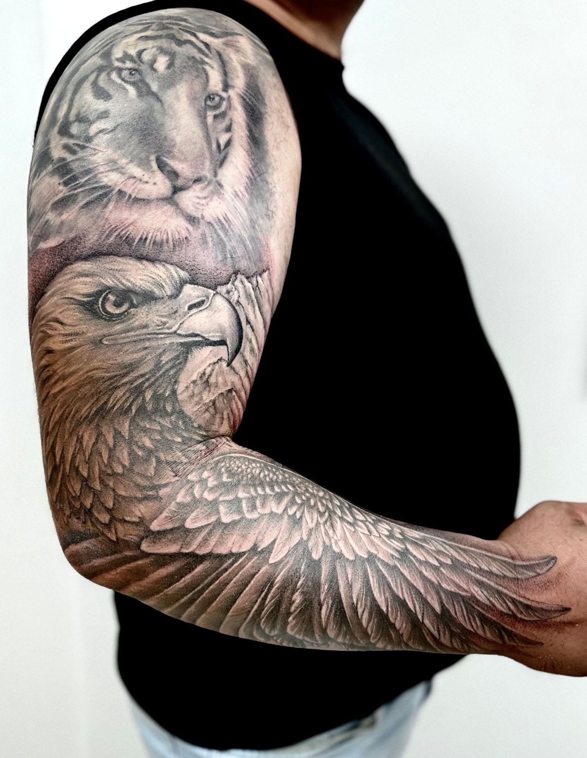 Black and grey eagle realism sleeve tattoo added below an existing tiger tattoo