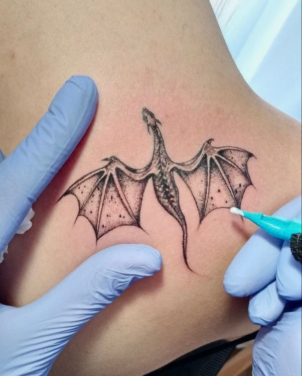 Fine line bat tattoo with open wings near the ankle