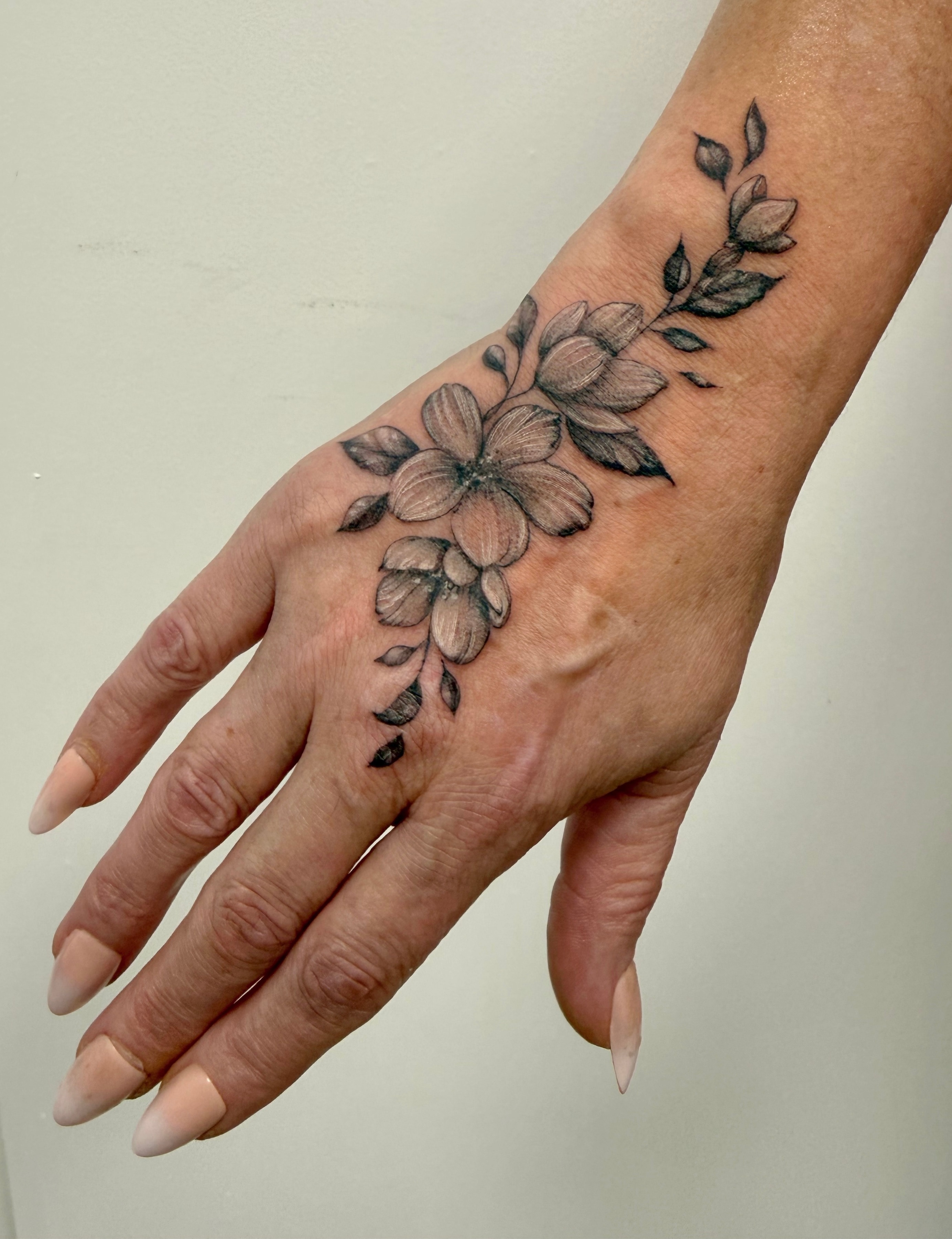 Black and grey flowers, buds and leaves running diagonally across the back of the hand and onto the wrist