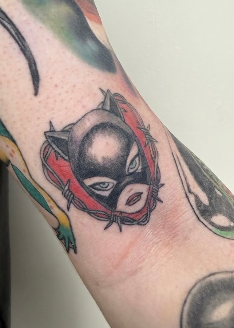 Old forearm tattoo of a masked face against a red background before the Iron Giant cover-up