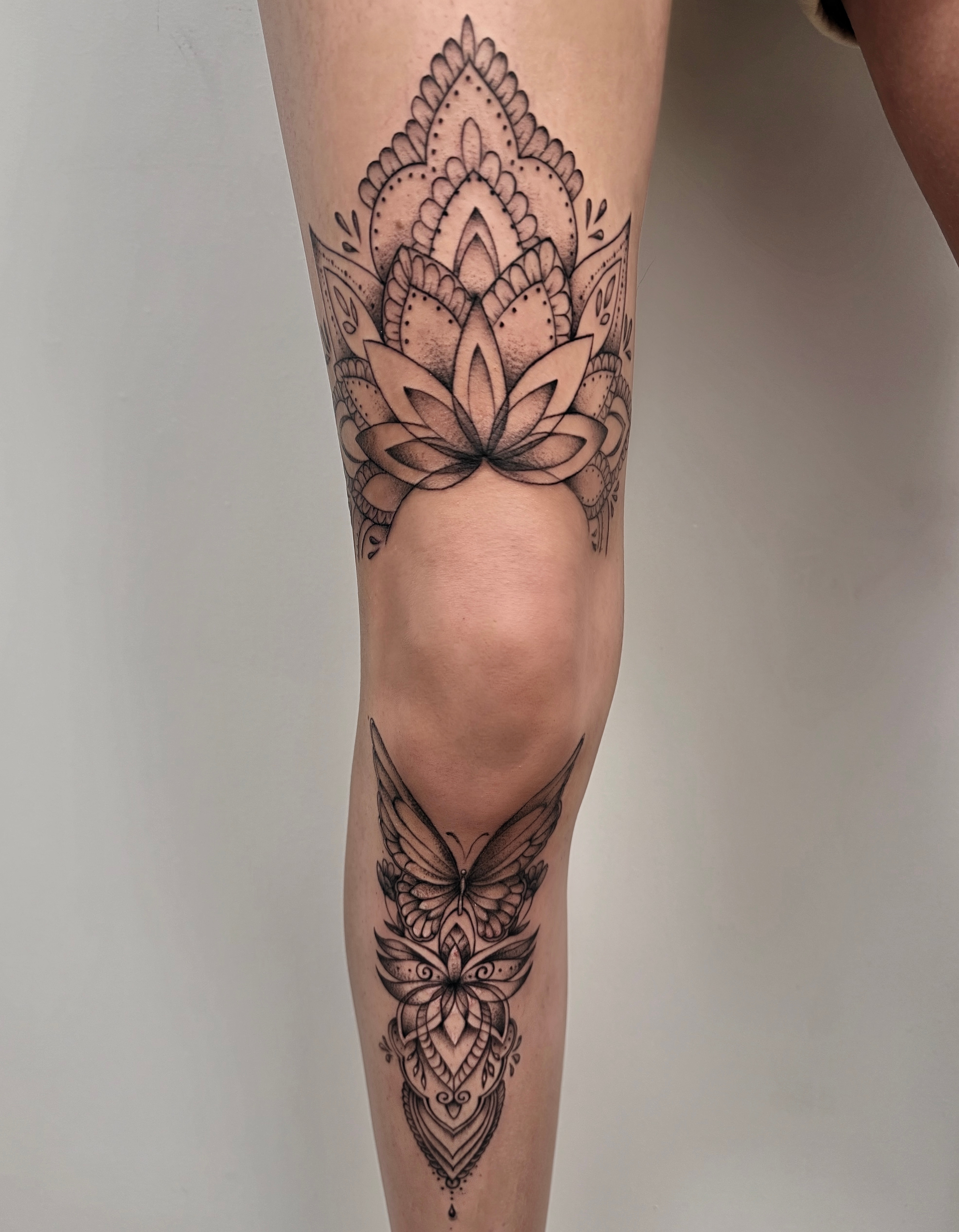 Black and grey lotus above the knee and butterfly on the shin, framed by ornamental patterns and dotwork