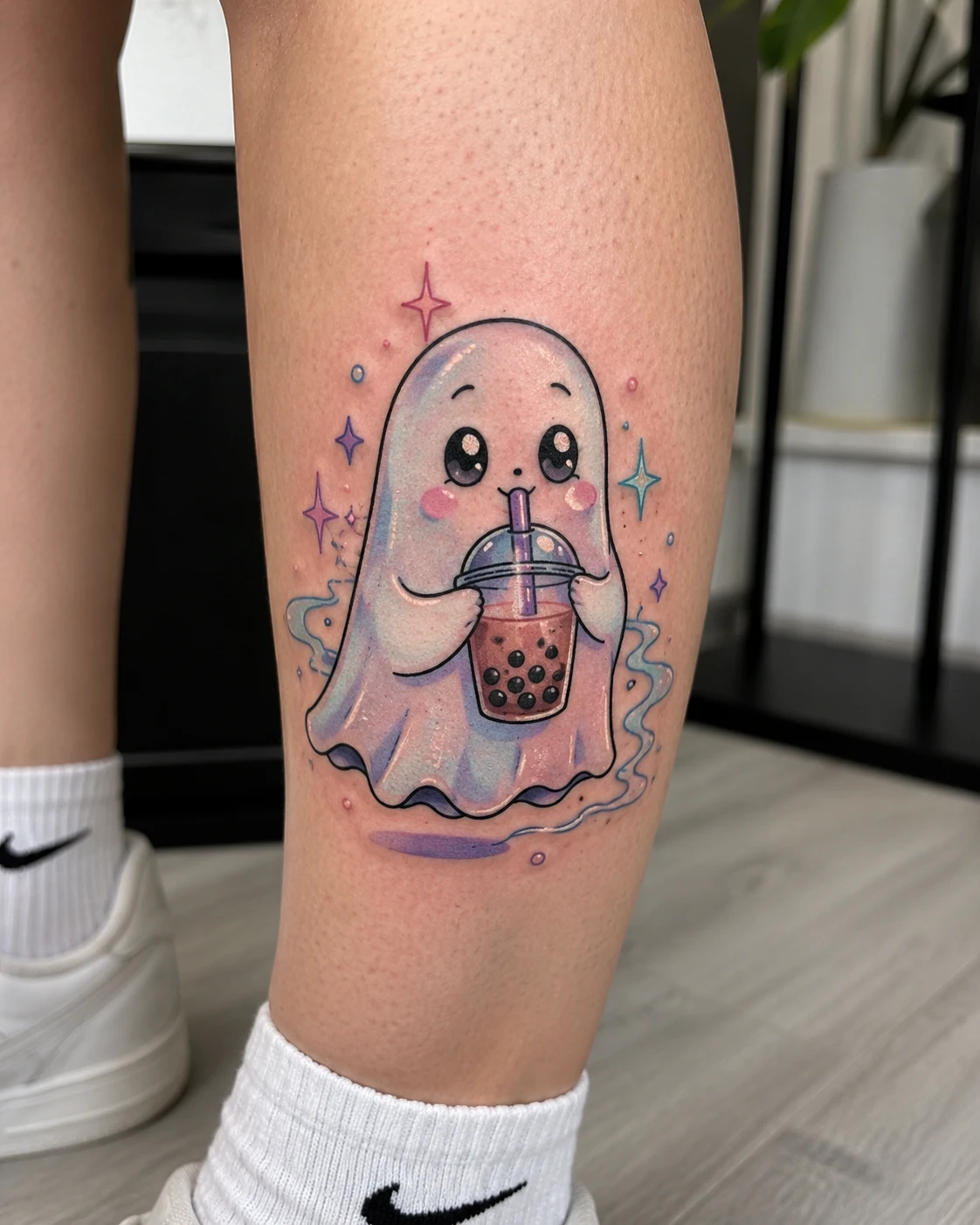 Rounded pastel ghost holding a bubble tea cup among four pointed sparkles, on a calf