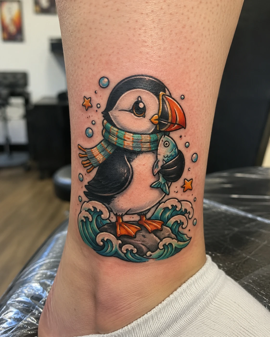 Puffin in a green scarf holding a fish among blue waves