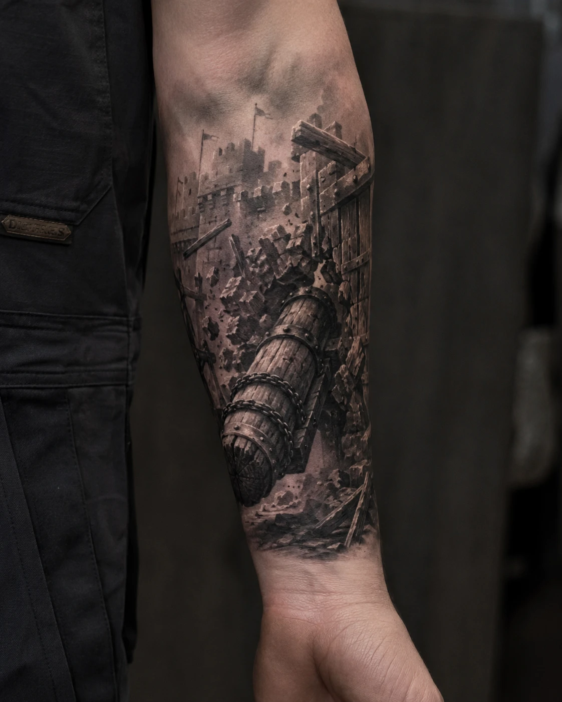 Battering ram breaking fortified castle gate tattoo on forearm
