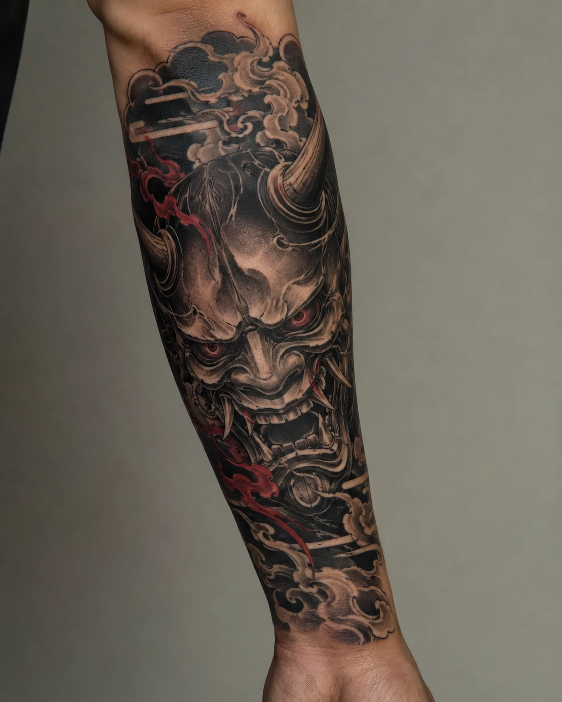Forearm tattoo of a Hannya mask, Japanese waves and clouds with red accents.
